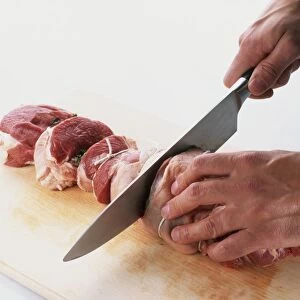 Cutting butterflied leg of lamb into steaks, using a large knife, close-up