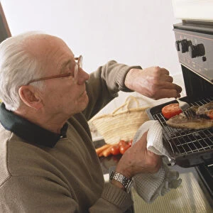 Elderly man cooking pork chop and tomato on a grill