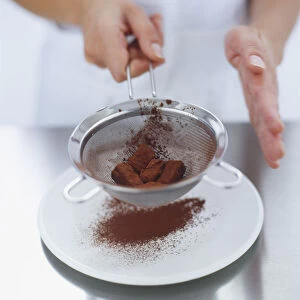 Excess cocoa powder being shaken off chocolate truffles in a sieve