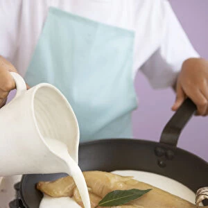Girl pouring milk into frying pan containing piece of haddock and bay leaf