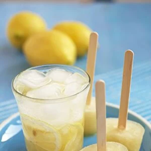 Glass of lemonade and three lemonade ice lollies on a plate, with fresh lemons in the background, close-up