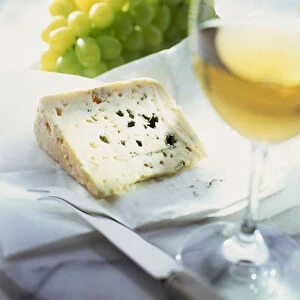 A glass of white wine and a dish of blue cheese and grapes in the background