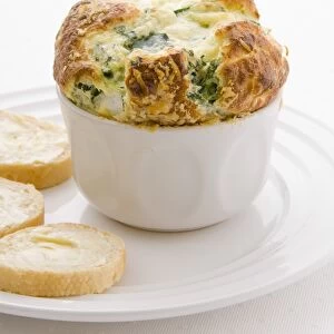 Golden puffy spinach souffle in bowl next to baguette slices