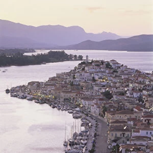 Greece, Poros, Poros town at sunset, harbour lights with boats moored, Peloponnese mountains in background