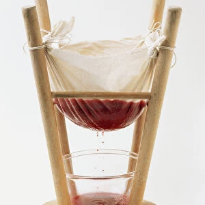 Jelly bag attached to upside down stool, raspberry jelly dripping into bowl below
