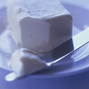 Knife with a small knob of butter, rests on glass dish