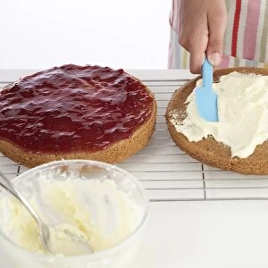 Making Victoria Sponge cake, spreading cream on top layer, close-up