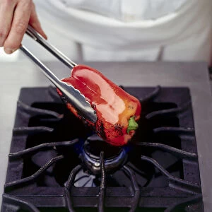 Man charring a red pepper by holding over an open flame using long-handled kitchen tongs