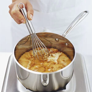 Metal whisk being used to stir butter and caramel syrup in saucepan, high angle view