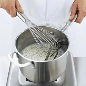 Metal whisk being used to stir milk and vanilla pods in saucepan, high angle view