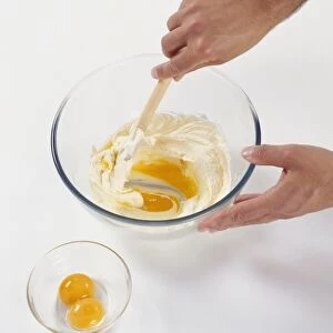 Mixing egg yolks into butter and sugar mixture using a wooden spoon, close-up