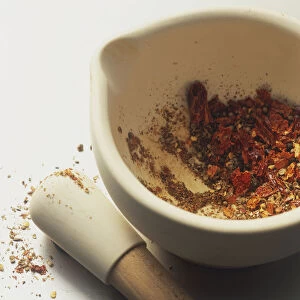 Mixture of dry spices, partly ground, at bottom of mortar, pestle lying by side