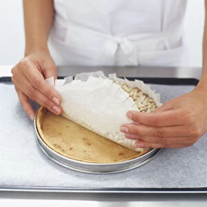 Paper lining filled with dried beans being rolled off partially baked tart pastry shell