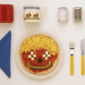 Pizza decorated as a smiley face, blue napkin, salt and pepper shakers, two mugs, knife and fork