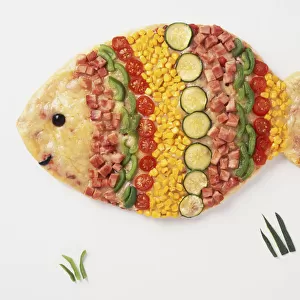 A pizza shaped like a fish with toppings of cheese, ham, sweetcorn, courgette, tomato, green bell pepper, and leaves as decoration