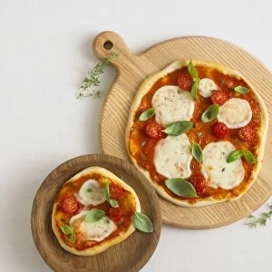 Two pizzas topped with mozzarella cheese, cherry tomatoes, basil and thyme leaves