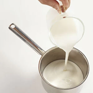 Pouring fresh cream from glass jug into saucepan, close-up