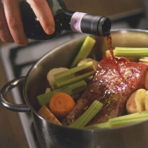 Red wine pouring out of bottle onto raw red meat and vegetables in a casserole (beef daube)