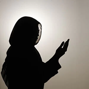 Silhouette of muslim woman in abaya prays with her hands up in air