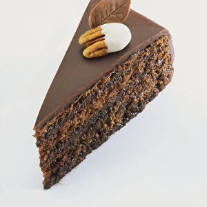 Slice of chocolate sponge cake coated with chocolate icing and decorated with chocolate leaf and nut