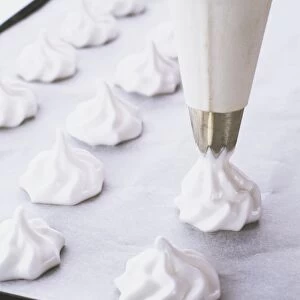 Small vanilla meringues being piped onto a baking sheet