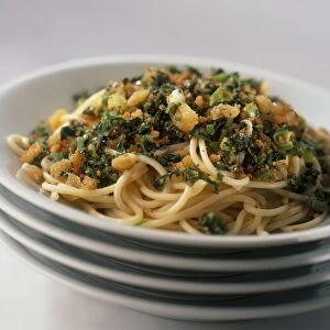 Spaghetti with herbs and breadcrumbs on stack of plates, close-up