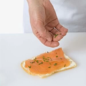 Sprinkling chives onto a smoked salmon and cream cheese sandwich