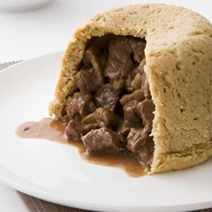 Steak and kidney pudding with stuffing showing, on a plate, close-up