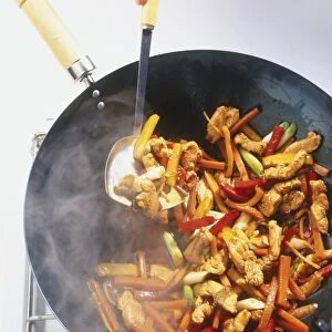 Stir-fried chicken with red peppers, yellow peppers, carrots and spring onions in a wok