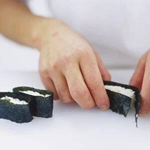 Sushi rice parcels being prepared with sheets of seaweed, close up