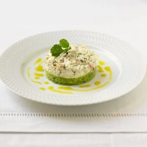 Tian of crab and avocado garnished with coriander leaf, on a plate