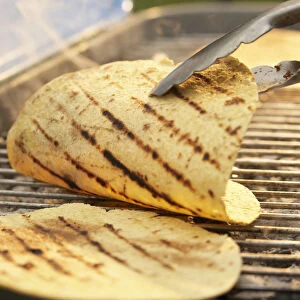 Tortillas on barbecue grill, being turned with tongs