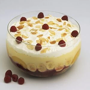 Trifle decorated with flaked almonds and raspberries, served in a glass bowl
