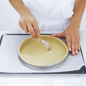 Using a fork to prick the base of pastry dough in a tart tin, high angle view