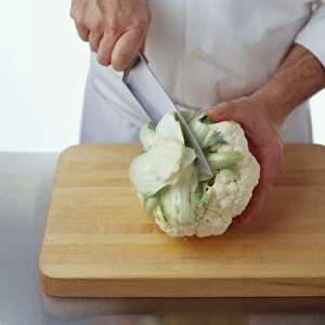 Using kitchen knife to cut stem base from cauliflower on chopping board