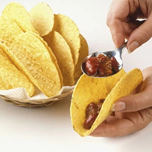 Using a spoon to fill a taco shell, close up
