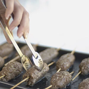 Using tongs to turn lamb kebabs on baking tray