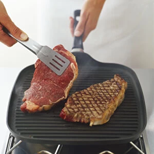 Using tongs to turn over steaks being char-grilled on a ridged, cast-iron grill pan