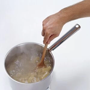 Using wooden spoon to stir rigatoni in saucepan of boiling water