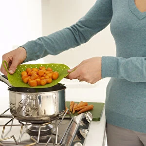 Woman using steamer filled with carrots over saucepan