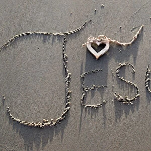 A wooden heart and the name of Jesus written in the sand