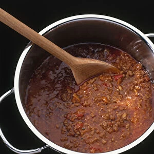 Wooden spoon stirring bolognese sauce in saucepan, view from above