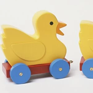Two yellow wooden toy ducks on wheels, side view