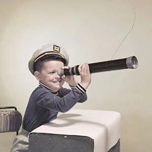 Boy wearing sailor hat looking through telescope, smiling