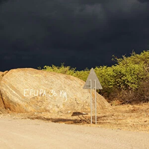 Dark storm front over rocks with signpost Epupa 36 km, Kaokoland, Kunene, Namibia