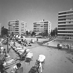 People relaxing at swimming pool surrounded by apartment buildings, (B&W)