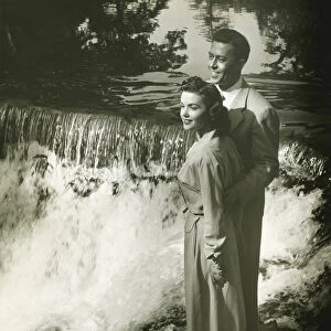 Young couple standing by waterfall, (B&W)