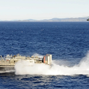 An SH-60F Seahawk helicopter follows a Landing Craft Air Cushiion in the Coral Sea