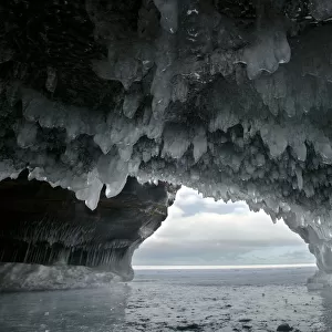 Ice hanging from arch in sea cave carved in soft sandstone cliffs, frozen lake, Squaw Bay
