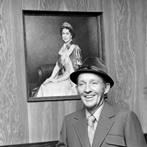 Bing Crosby pictured in the exclusive tailors shop infront of a portrait of HM The